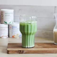 Un verre de matcha chaud, mousseux et crémeux, prêt à être dégusté. À côté, une carafe de lait végétal.