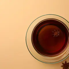 Une tasse de thé ambré avec une étoile d'anis flottant à l'intérieur. Autour, plusieurs étoiles d'anis, rappelant le danger potentiel de l'anis étoilé japonais.