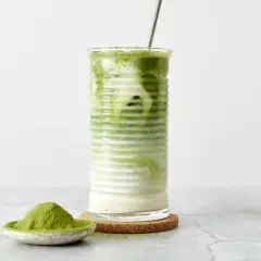 Un verre de matcha frappé, crémeux et rafraîchissant, avec une cuillère de poudre de matcha à côté.