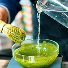 Préparation d'un matcha apaisant pour l'intestin irritable. Un fouet en bambou est utilisé pour mélanger la poudre verte dans un bol.
