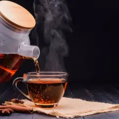 Un thé noir fumant est versé d'une théière en verre dans une tasse. Parfait pour un thé noir le soir, avec des bâtons de cannelle et de l'anis étoilé.