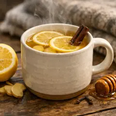 Une tasse fumante de grog sans alcool, garnie de rondelles de citron et d'un bâton de cannelle, avec du miel et du gingembre à proximité.