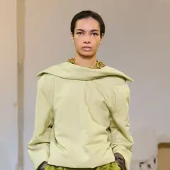 Mannequin portant un haut ample couleur matcha, avec un collier doré audacieux et une jupe texturée verte.