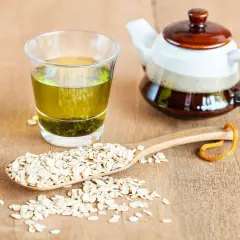 Verre de thé vert, théière et cuillère en bois remplie de flocons d'avoine. Découvrez les mugicha bienfaits pour une boisson rafraîchissante.