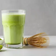 Un verre de matcha crémeux, une cuillère de poudre verte et un fouet traditionnel. Idéal pour une femme enceinte cherchant une boisson saine.