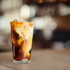 Un verre de latte glacé avec des tourbillons de crème dans le café sombre, sur un comptoir.