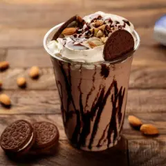 Un délicieux milkshake vegan au chocolat, garni de crème, d'amandes et de biscuits, sur fond de bois.