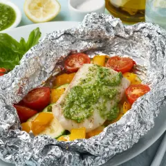 Un délicieux poisson en papillote, garni de légumes colorés et d'une sauce verte savoureuse, prêt à être dégusté.
