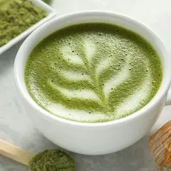 Un délicieux café matcha latte, orné d'une mousse crémeuse et d'une pincée de poudre de matcha sur une cuillère en bois.