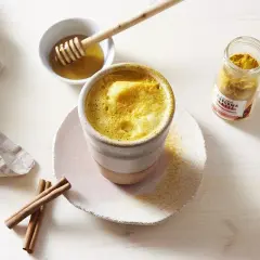 Un golden latte crémeux, prêt à déguster. Découvrez les golden latte bienfaits pour une pause réconfortante et saine. Miel et curcuma à portée de main.