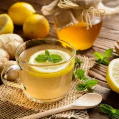 Une tasse de thé chaud au citron et à la menthe, avec du ginseng gingembre râpé, des citrons entiers et un pot de miel.