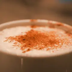 Une tasse blanche remplie d'une boisson crémeuse, saupoudrée de cannelle. Une parfaite composition chai latte pour un moment de détente.