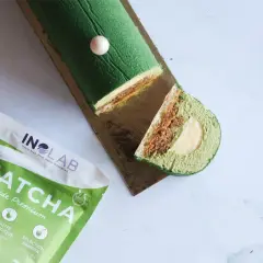 Bûche glacée verte au matcha, garnie d'une ganache matcha crémeuse et d'une surprise au centre. À côté, un paquet de poudre de matcha de qualité premium.