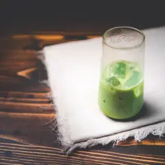 Un verre de matcha glacé sur un tissu blanc, sur fond de bois sombre. Une boisson rafraîchissante pour se demander : peut-on boire du matcha le soir ?