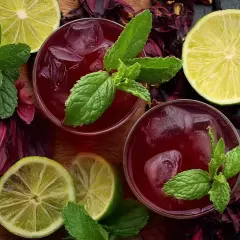 Deux verres de bissap chaud, décorés de menthe fraîche, de citrons verts et de fleurs d'hibiscus séchées.