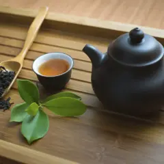 Service à thé en bambou avec théière noire, tasse de thé ambré, feuilles de thé et une branche de feuilles vertes. Parfait pour un thé sans théine.