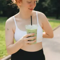 Une jeune femme aux taches de rousseur tient une boisson verte glacée, un rituel quotidien pour elle : boire du matcha.