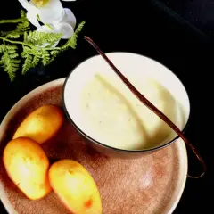 Un bol de lait vanille onctueux, garni d'une gousse de vanille, avec des madeleines dorées sur une assiette.