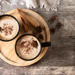 Deux tasses de chai latte réconfortant, garnies d'anis étoilé et de cannelle, sur un plateau en bois.