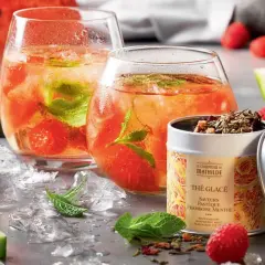 Deux verres de thé glacé maison aux fruits rouges et menthe, accompagnés de pastèque, framboises et d'une boîte de thé.