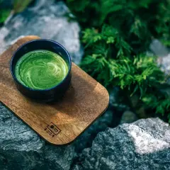 Tasse de matcha crémeux sur un plateau en bois, entourée de rochers et de verdure. Idéal pour des matcha recettes salées.