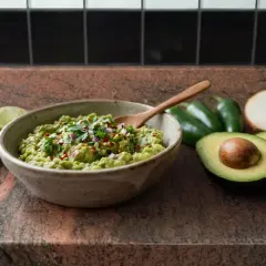 Un délicieux rougail avocat frais, garni de coriandre et d'oignons rouges, prêt à être dégusté avec des jalapeños et des citrons verts.