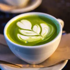 Un délicieux matcha lait d'avoine avec un art latte en forme de feuille, servi dans une tasse blanche sur une soucoupe.