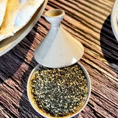 Un bol de zaatar prêt à être utilisé pour une recette, avec du pain pita et une trempette crémeuse.