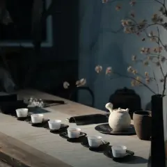 Service à thé minimaliste avec tasses blanches alignées. Une théière en céramique et un vase de fleurs séchées évoquent l'art de comment conserver le thé.