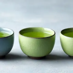 Trois tasses de thé vert vif, une bleue et deux vertes, suggérant la dose maximale de thé vert par jour pour une dégustation paisible.