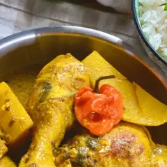 Un plat de poulet au curry, parfumé par l'épice colombo, avec des morceaux de patate douce et un piment rouge. Servi avec du riz blanc.