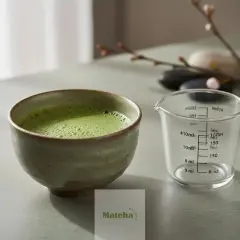 Un bol de matcha mousseux et une tasse à mesurer graduée, prêts pour vous montrer comment faire un matcha parfait.
