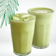 Deux verres de matcha lait de coco, l'un glacé avec des glaçons, l'autre onctueux, sous une feuille de palmier stylisée.