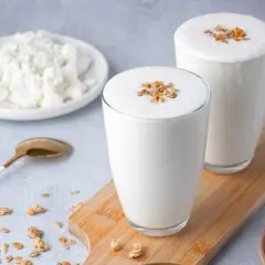 Deux verres de kefir de lait crémeux, garnis de granola, à côté d'une assiette de fromage blanc et d'une cuillère dorée.