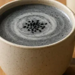 Une tasse de latte au sésame noir, garnie de graines de sésame, avec une cuillère à proximité.
