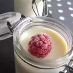 Délicieux panna cotta chocolat blanc, garni d'une framboise givrée, dans un pot en verre.