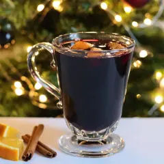 Verre de vin chaud sans alcool, garni d'orange et de cannelle, devant un sapin de Noël illuminé. Parfait pour une recette festive et réconfortante.