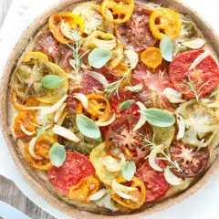 Tarte tomate claire au matcha, garnie de tomates multicolores, oignons, ail, romarin et basilic frais. Une œuvre culinaire colorée et savoureuse.