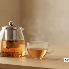 Une théière en verre fumante et une tasse de thé ambré sur une table en bois. Le temps idéal pour savoir combien de temps infuser le thé pour une saveur parfaite.