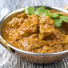 Un savoureux colombo d'agneau, mijoté dans une sauce épicée et garni de coriandre fraîche, servi dans un bol en cuivre.