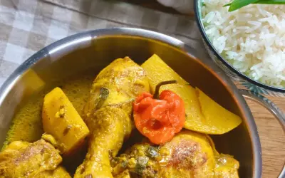 Un plat de poulet au curry, parfumé par l'épice colombo, avec des morceaux de patate douce et un piment rouge. Servi avec du riz blanc.
