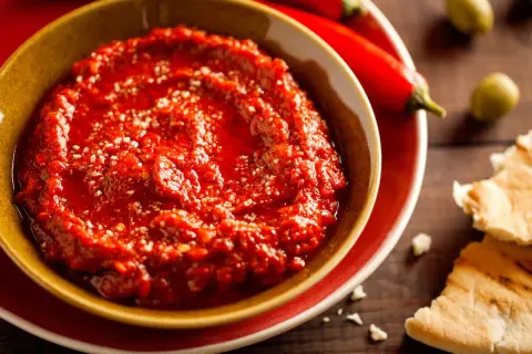 Un bol de harissa maison, prêt à être dégusté avec du pain pita. Une recette simple pour un goût authentique.