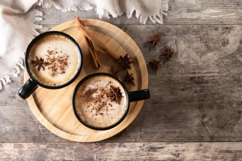 Deux tasses de chai latte réconfortant, garnies d'anis étoilé et de cannelle, sur un plateau en bois.