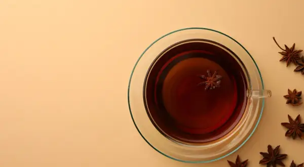 Une tasse de thé ambré avec une étoile d'anis flottant à l'intérieur. Autour, plusieurs étoiles d'anis, rappelant le danger potentiel de l'anis étoilé japonais.