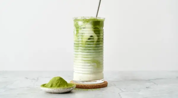 Un verre de matcha frappé, crémeux et rafraîchissant, avec une cuillère de poudre de matcha à côté.
