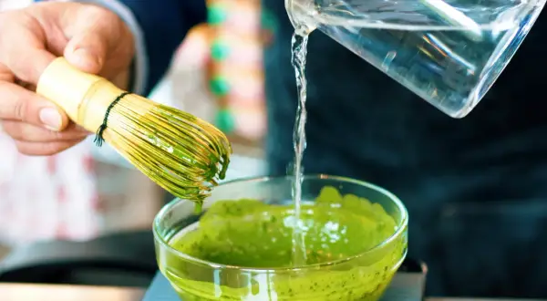 Préparation d'un matcha apaisant pour l'intestin irritable. Un fouet en bambou est utilisé pour mélanger la poudre verte dans un bol.