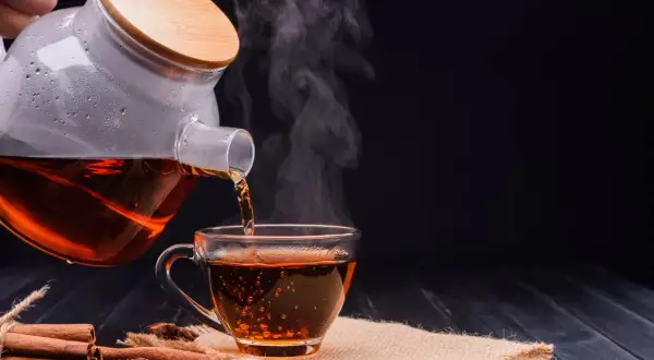 Un thé noir fumant est versé d'une théière en verre dans une tasse. Parfait pour un thé noir le soir, avec des bâtons de cannelle et de l'anis étoilé.
