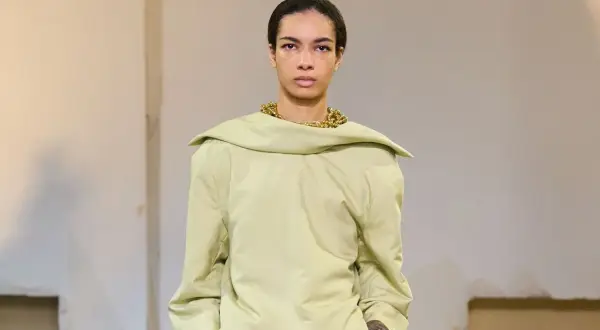 Mannequin portant un haut ample couleur matcha, avec un collier doré audacieux et une jupe texturée verte.