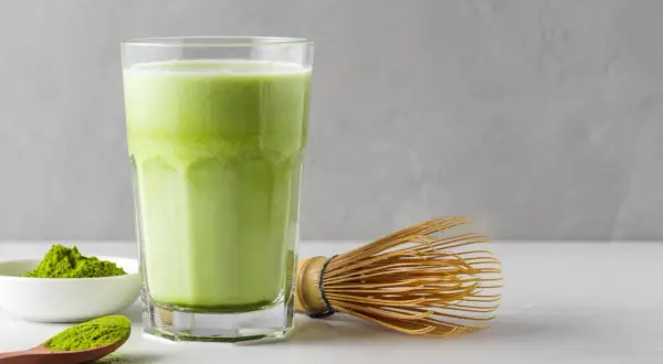 Un verre de matcha crémeux, une cuillère de poudre verte et un fouet traditionnel. Idéal pour une femme enceinte cherchant une boisson saine.