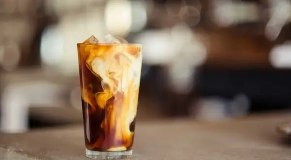 Un verre de latte glacé avec des tourbillons de crème dans le café sombre, sur un comptoir.